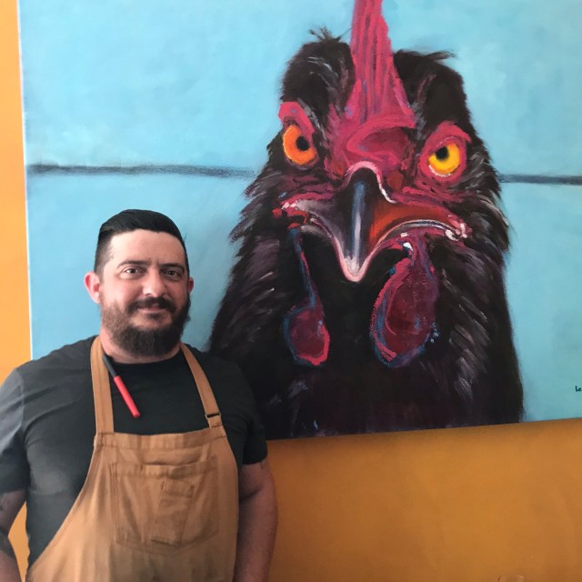 Chef Kyle chef looking at camera with chicken painting in background
