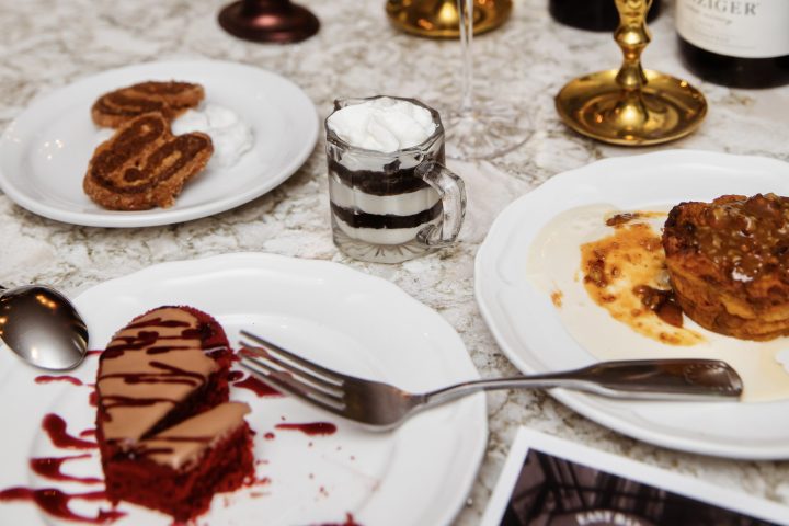 Dessert plates with red velvet cake, cookies and drinks on a table with candles.