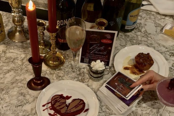 Table setting with candles, wine bottles, plates of desserts, and a glass of champagne.