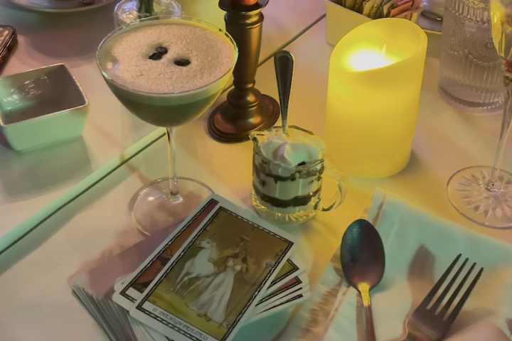 Candlelit table with espresso martini, tarot cards, flowers, and cutlery.