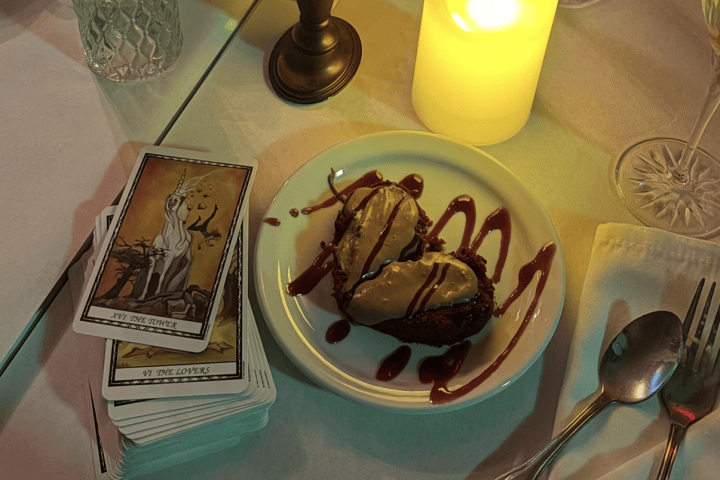 Candlelit table with dessert, tarot cards, and floral vase.