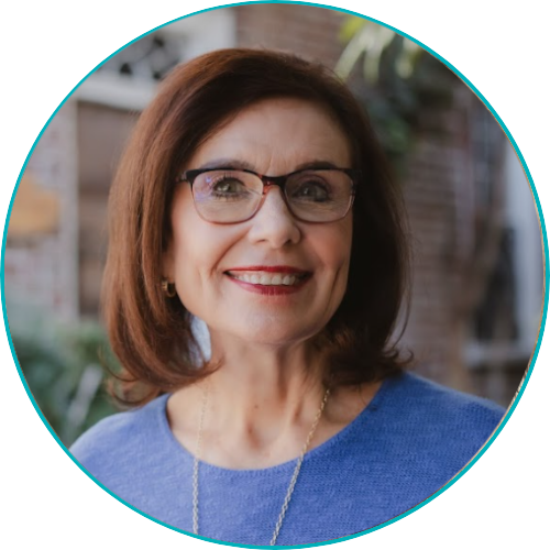 Smiling woman with glasses, brown hair, wearing a blue top, standing outdoors.