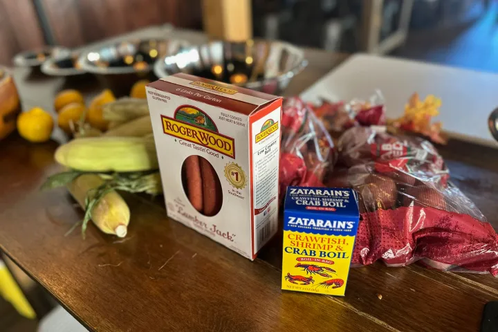 Ingredients on a table including sausages, corn, seasoning, and red potatoes.