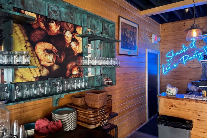 Wooden interior of a restaurant with neon sign, shrimp photo, and glass jars on shelves.