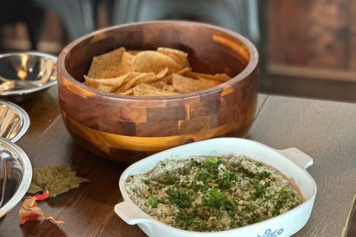 Wood bowl with tortilla chips and white dish with dip on wooden table.