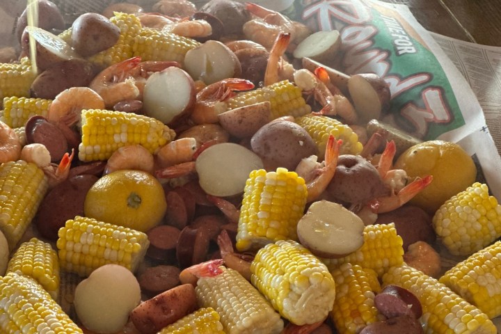Seafood boil with corn, potatoes, sausage, and shrimp on newspaper-covered table.